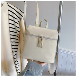 Detail of cream nylon backpack featuring dual zippers and sturdy rounded top handle