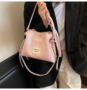 Detail shot of light pink drawstring bucket bag with a decorative logo and chain strap