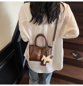 Close-up of brown crocodile texture handbag with horse charm on a wooden staircase