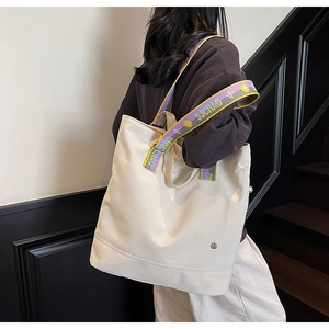 Detail of off-white canvas tote bag featuring a wide colorful striped lettered shoulder strap