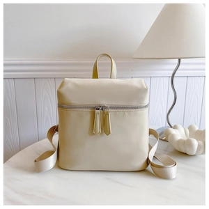 Detail of a minimalist beige nylon backpack with double zipper closure on marble surface