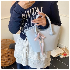 Détail du sac seau en cuir bleu clair avec ruban rose et breloque en perles