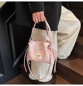 Detailed shot of a pink drawstring bucket bag with a branded patch and metal chain strap