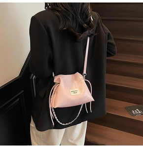Detail shot of a light pink drawstring bucket bag with chain strap on a model