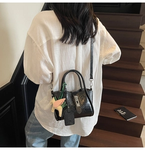 Detail of black crocodile pattern handbag with silver lock and Pegasus charm on stairs
