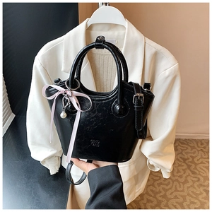 Détail du sac seau noir avec un nœud en soie rose et un pendentif perle