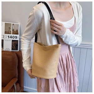 Detailed view of beige straw bucket bag with black leather strap on female model