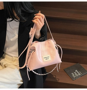 Detail of pink matte leather bucket bag with chain strap and branding on wooden stairs