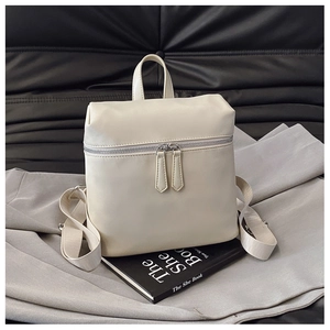 Detail of minimalist cream PU leather backpack with silver zippers on a black background