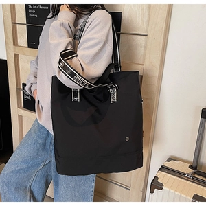 Detail of black nylon tote bag with jacquard SJCHAO strap shown in a travel setting