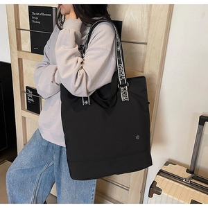 Detail of black tote bag with lettered woven straps and metal logo in indoor scene