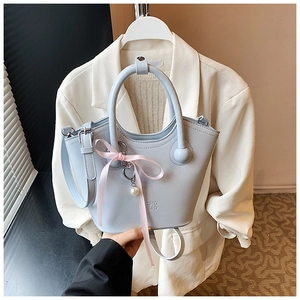 Détail du sac cabas bleu clair avec un nœud en soie rose et un pendentif en perles de cœur