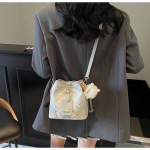 Detailed shot of a light grey jacquard bucket bag with plush charm on a shoulder strap