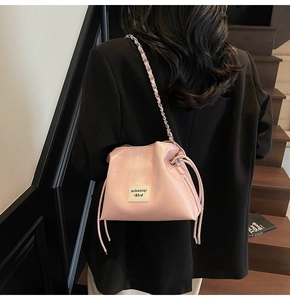 Pink drawstring bucket bag with silver metal chain strap worn by a model in a black blazer