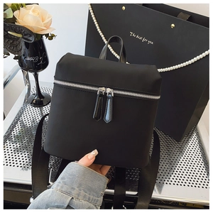 Detail of a minimalist black backpack with silver zippers and wide woven straps
