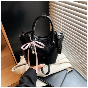 Détail du sac seau en cuir verni noir avec nœud en satin rose et breloques de perles