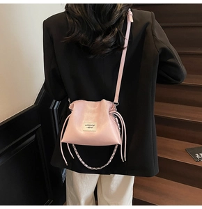 Detailed view of pink drawstring bucket bag with logo patch and metal chain strap