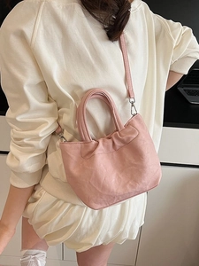 Pink pleated bucket bag with round handle and detachable strap on model in cozy interior