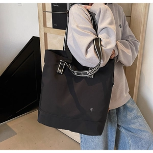 Detail of black tote bag featuring jacquard webbing strap and circular metal logo