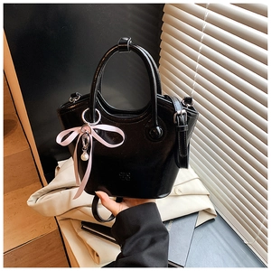 Détail d'un sac seau en cuir verni noir avec ruban rose et breloque en perle sur la lanière