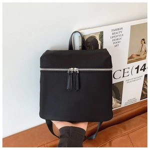 Detail of a black nylon backpack with silver zipper and long leather pullers
