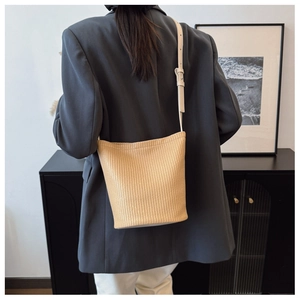 Detailed view of beige woven bucket bag worn with a professional grey blazer and white trousers