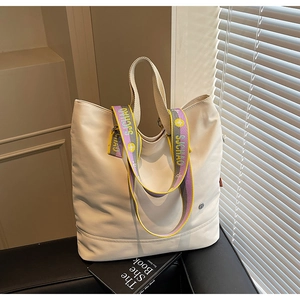 Detail of cream tote bag featuring a colorful patterned strap and soft leather texture