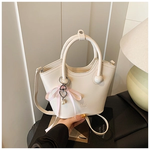 Détail du sac seau en cuir crème avec poignée ronde et breloque en ruban perlé