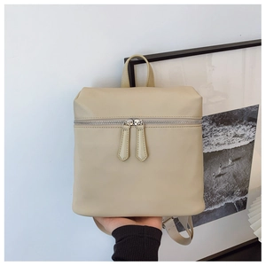 Detail of a beige PU leather backpack featuring dual silver zippers and adjustable straps
