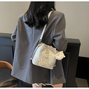 Detail view of the geometric embossed pattern and plush charm on the white bucket bag