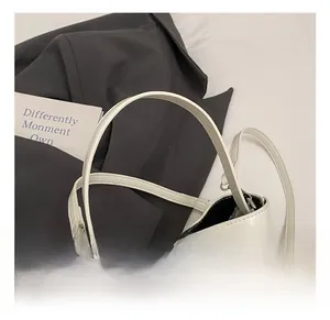 Detail of white glossy leather bucket bag with wide handle and metal eyelet accents