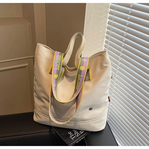 Close-up of cream canvas tote bag with a colorful striped wide shoulder strap on black leather
