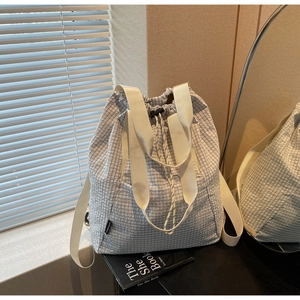 Detail of light grey checkered drawstring tote bag with dual straps and brand tag