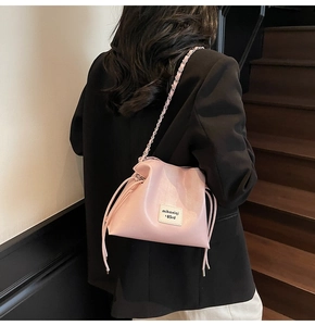 Close-up of light pink pebble leather bucket bag with silver metal chain and braided strap