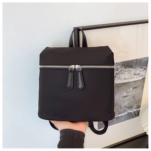 Detail of a black nylon backpack featuring smooth fabric and dual silver metal zippers
