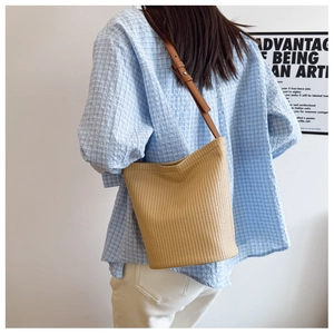 Detail of a beige woven bucket bag with brown leather strap worn by a model