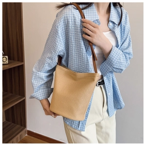 Close-up of woven straw bucket bag with dark brown leather strap and natural texture