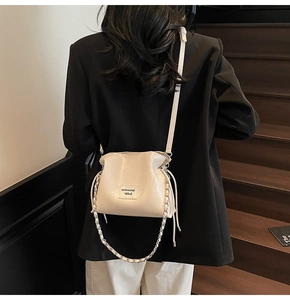 Close-up of stylish off-white bucket bag with drawstring and chic leather chain detail