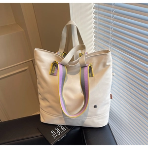 Detail of white canvas tote bag with purple striped handle and metallic logo on side