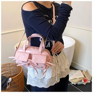 Gros plan du sac bowling en cuir verni rose avec détails nœuds et poches avant