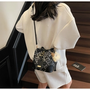 Detail of geometric pattern bucket bag with leather strap and plush charm on wooden stairs
