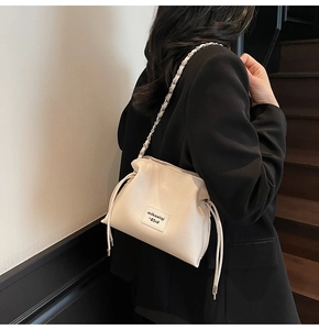 Detail of a creamy white crossbody bucket bag with chain strap and letter patch