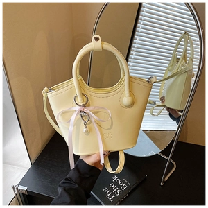 Détail du sac seau en cuir jaune clair avec ruban rose et breloque perle en cœur