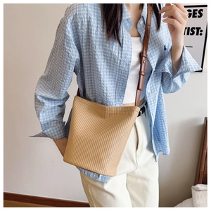Straw bucket bag detail featuring woven texture and brown leather adjustable shoulder strap