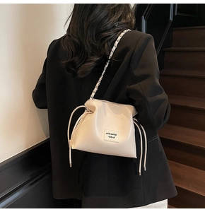 Close-up of cream drawstring bucket bag with chain strap worn over a black blazer