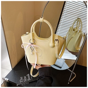 Détail du sac seau jaune pâle avec un nœud en ruban rose et pendentif perle