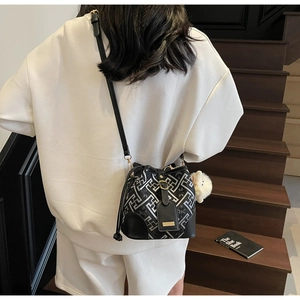 Detail of a black and silver bucket bag with geometric patterns and white pom-pom charm