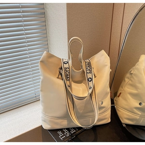 Detail view of a large cream tote bag with decorative patterned shoulder strap and handles