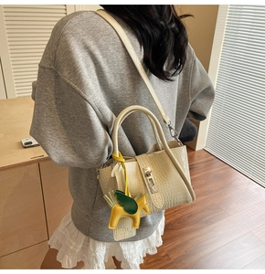 Detail of beige crocodile embossed handbag with detachable strap and horse charm