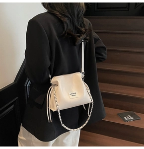 Close-up of creamy white bucket bag with chain strap worn by model in a suit
